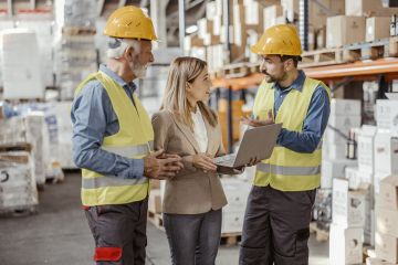 Warehouse staff in discussion wearing hi vis jackets and helmets.