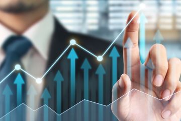 Close-up of a hand pointing to a rising graph line with upward arrows, symbolizing business growth and financial success.