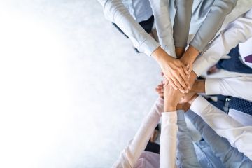 Group of diverse, business people with arms centred showing unity and teamwork.