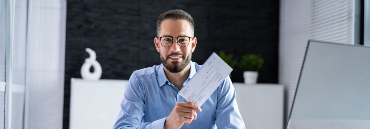 Man in blue shirt in office holding pay related document.